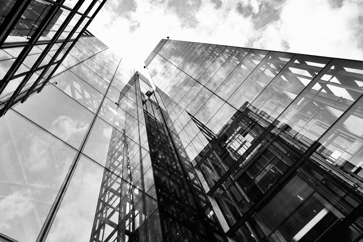 Organisation & Struktur - Ansicht eines Hochhauses von unten, in der Glasfassade spiegeln sich Wolken