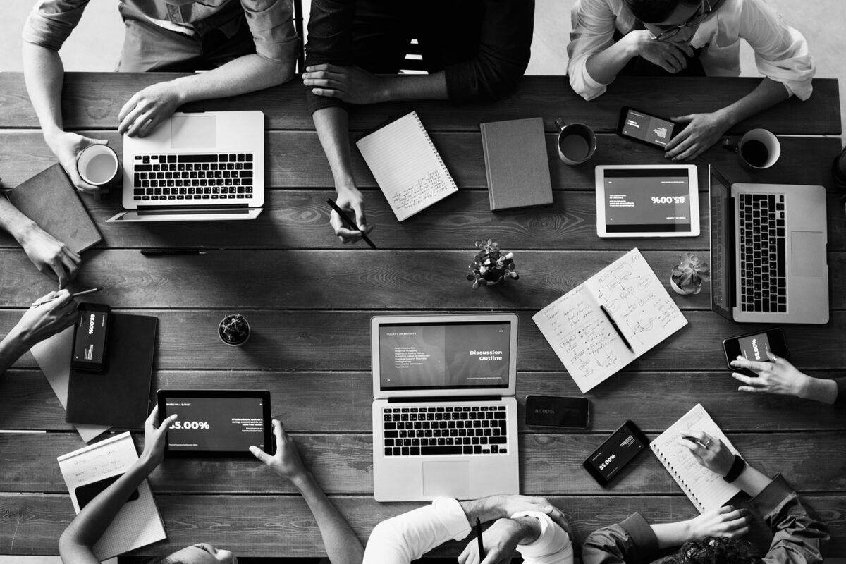 Projekte - Mehrere Personen sitzen mit Laptops und Notizbüchern an einem Tisch und besprechen sich