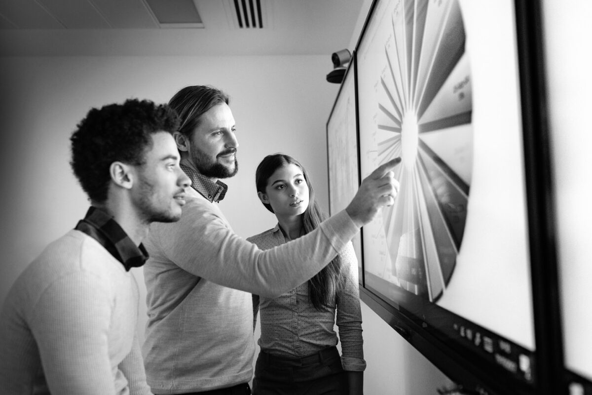 Technologie wirksam machen - Drei Personen stehen vor einem Touchscreen und studieren eine Grafik