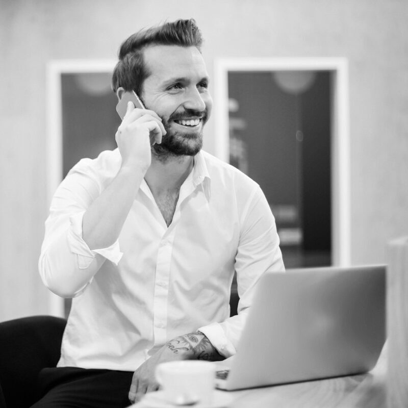 Kultur und Führung -quadrat- Ein Mann sitzt vor seinem Laptop und telefoniert mit seinem Mobiltelefon