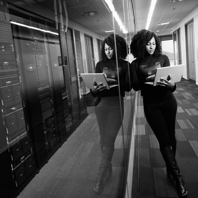 Technologie und Infrastruktur -quadrat- Frau mit Laptop steht vor einem gläsernen Serverschrank